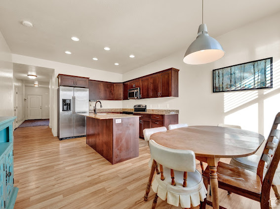 Kitchen featuring light hardwood / wood-style floors, hanging light fixtures, an island with sink, stainless steel appliances, and dark brown cabinetry