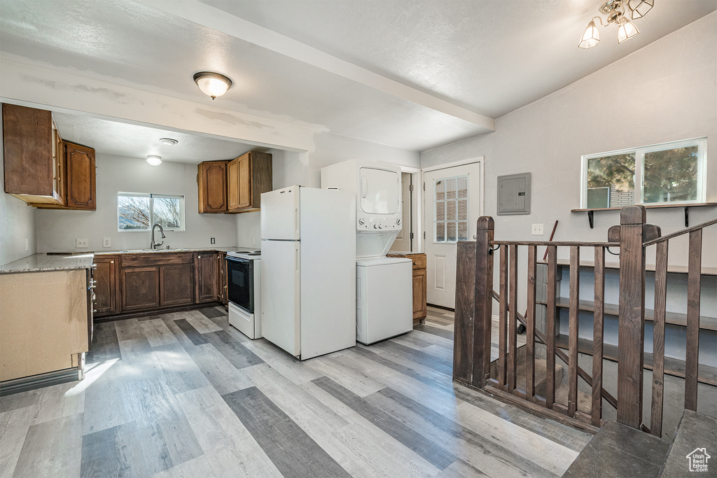 Kitchen with white appliances, light hardwood / wood-style flooring, stacked washer and dryer, and sink