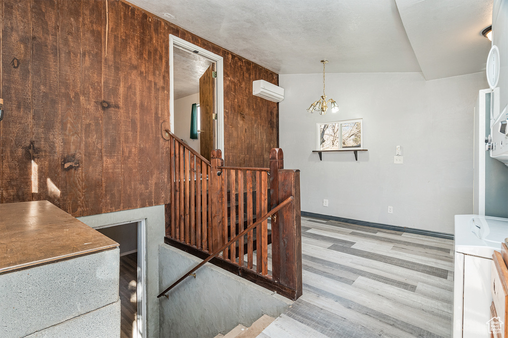 Stairs featuring light hardwood / wood-style floors, a wall mounted air conditioner, an inviting chandelier, and wooden walls