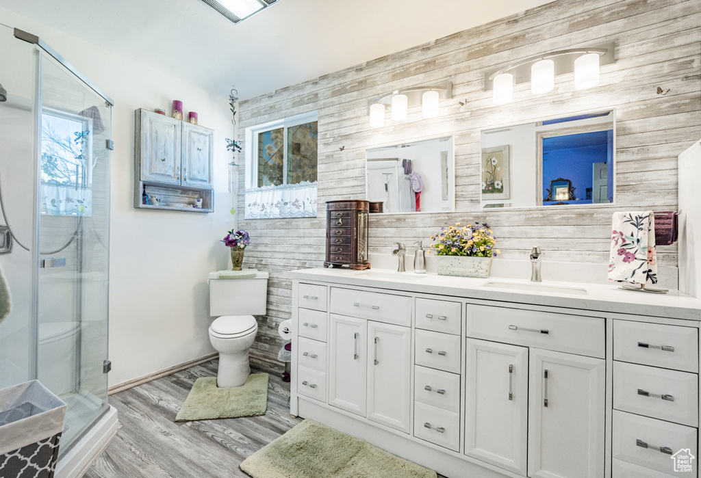 Bathroom featuring vanity with extensive cabinet space, hardwood / wood-style flooring, toilet, wooden walls, and a shower with shower door