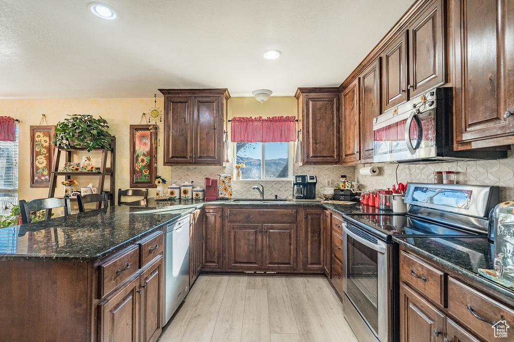 Kitchen with backsplash, light wood-type flooring, sink, stainless steel appliances, and dark stone countertops