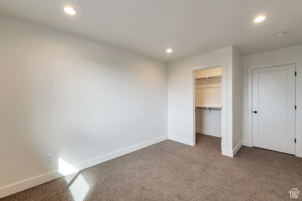 Unfurnished bedroom with a spacious closet, dark carpet, and a closet