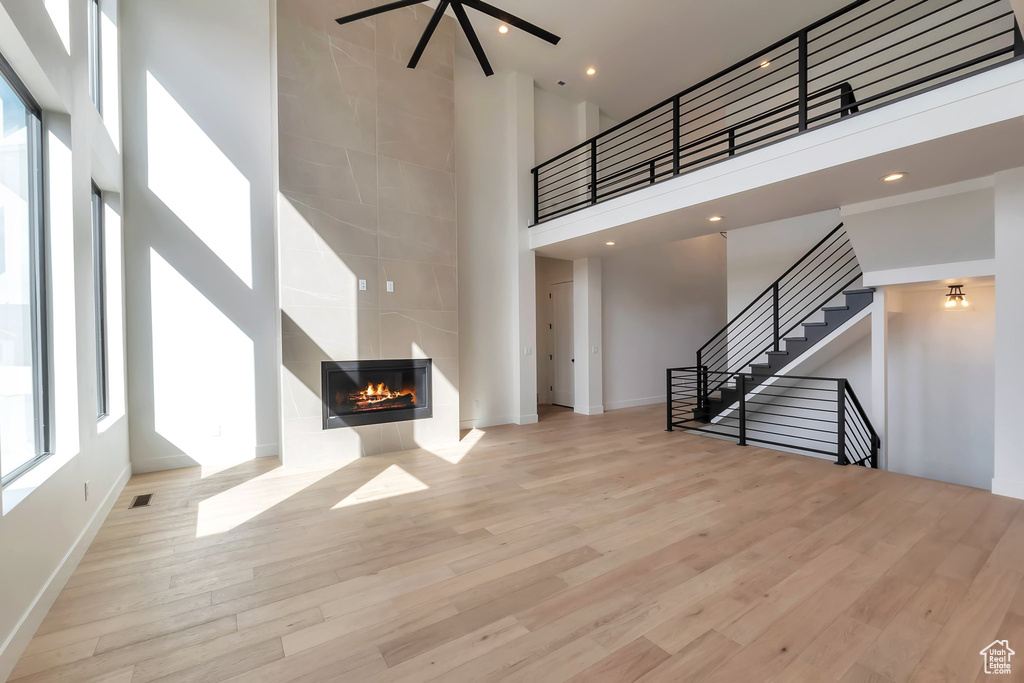 Unfurnished living room with light hardwood / wood-style flooring, a fireplace, and a towering ceiling