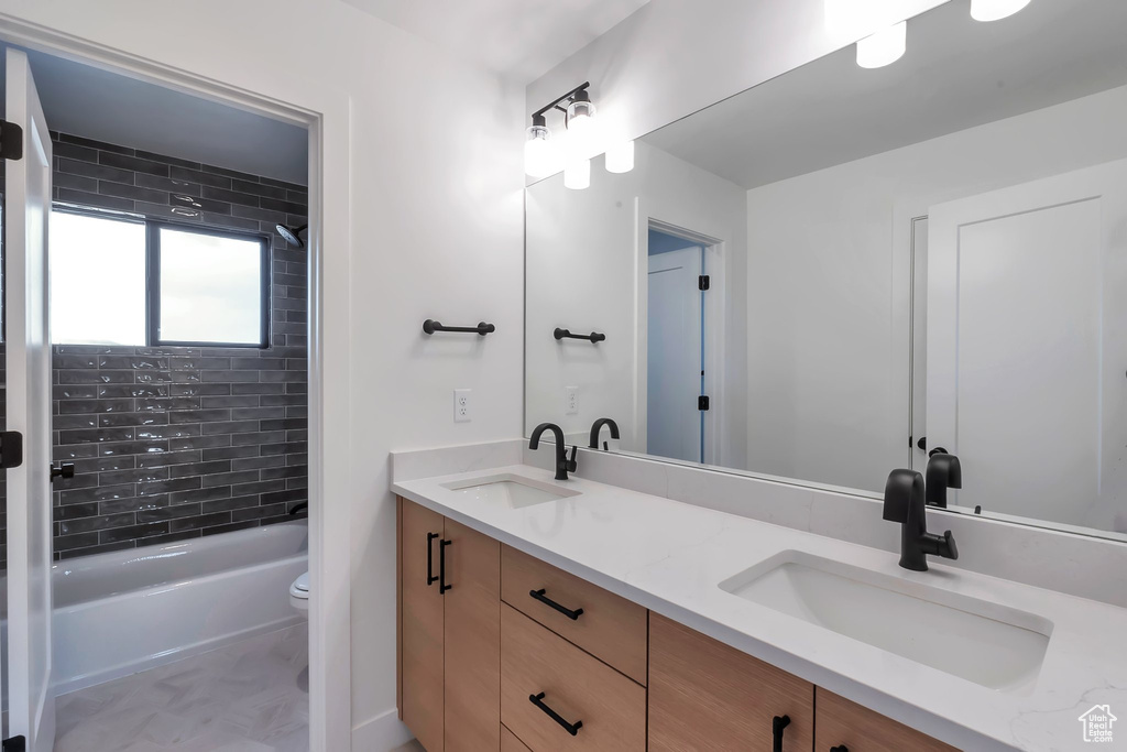 Full bathroom featuring dual vanity, tiled shower / bath combo, tile floors, and toilet
