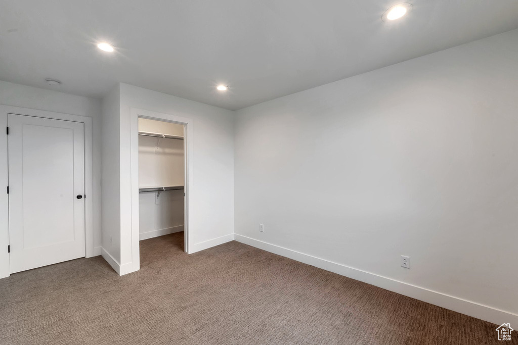 Unfurnished bedroom with a closet, dark colored carpet, and a walk in closet