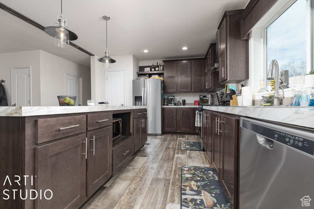 Kitchen featuring dark brown cabinets, light stone counters, appliances with stainless steel finishes, light hardwood / wood-style flooring, and decorative light fixtures
