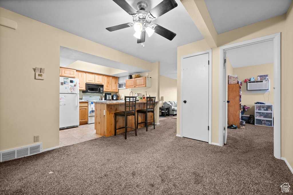 Kitchen featuring an AC wall unit, ceiling fan, a breakfast bar, white appliances, and light colored carpet