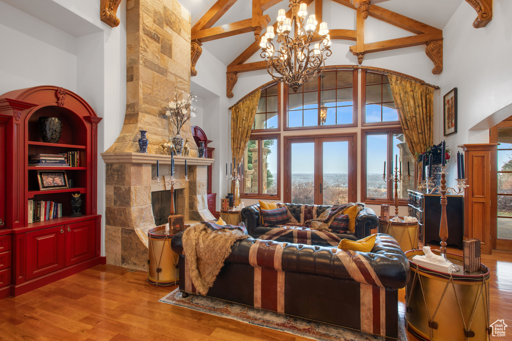 Living room with a stone fireplace, hardwood / wood-style flooring, a notable chandelier, and high vaulted ceiling