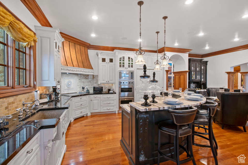 Kitchen with light hardwood / wood-style flooring, a kitchen island, custom range hood, tasteful backsplash, and appliances with stainless steel finishes