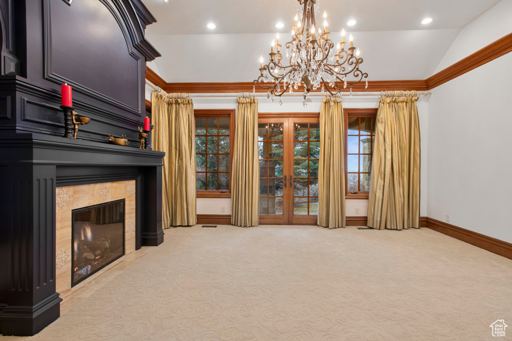 Unfurnished living room featuring an inviting chandelier, a fireplace, crown molding, light colored carpet, and lofted ceiling