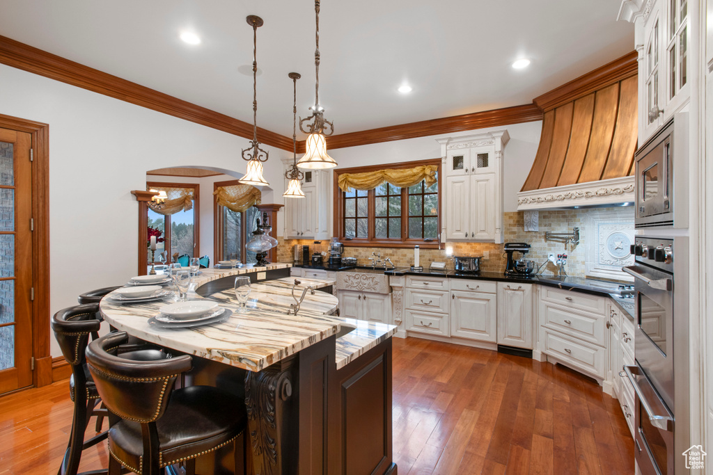 Kitchen with backsplash, a center island, dark wood-type flooring, premium range hood, and pendant lighting
