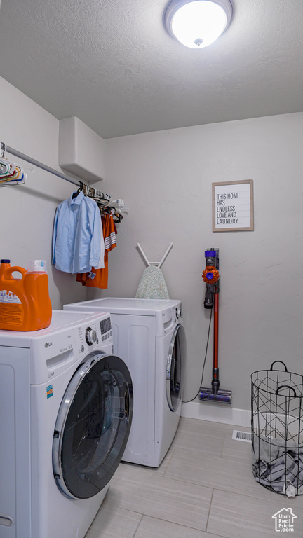 Laundry room featuring light tile floors, a textured ceiling, and independent washer and dryer