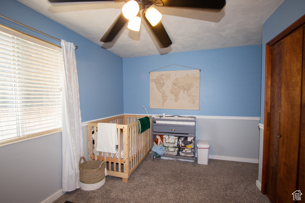 Bedroom with ceiling fan, a crib, a closet, and dark carpet