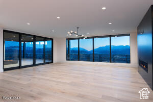 Unfurnished living room with light hardwood / wood-style flooring, a mountain view, a notable chandelier, and a wall of windows