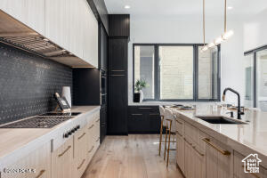 Kitchen featuring light wood-type flooring, backsplash, a kitchen bar, hanging light fixtures, and sink