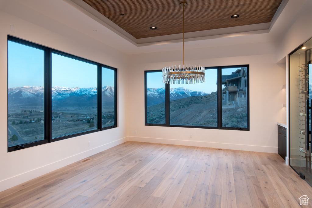 Unfurnished room featuring a mountain view, light hardwood / wood-style flooring, wooden ceiling, and a raised ceiling