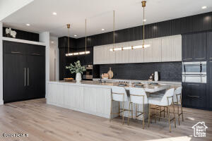 Kitchen featuring decorative light fixtures, tasteful backsplash, wall oven, a kitchen island, and light hardwood / wood-style floors