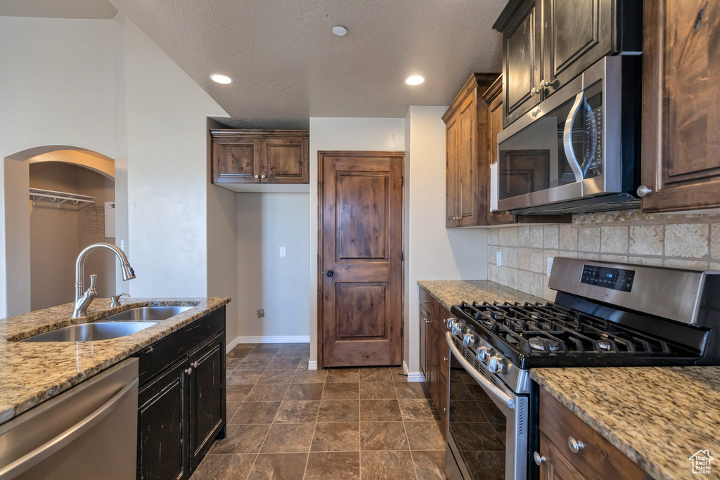 Kitchen with stainless steel appliances, light stone counters, backsplash, dark tile flooring, and sink