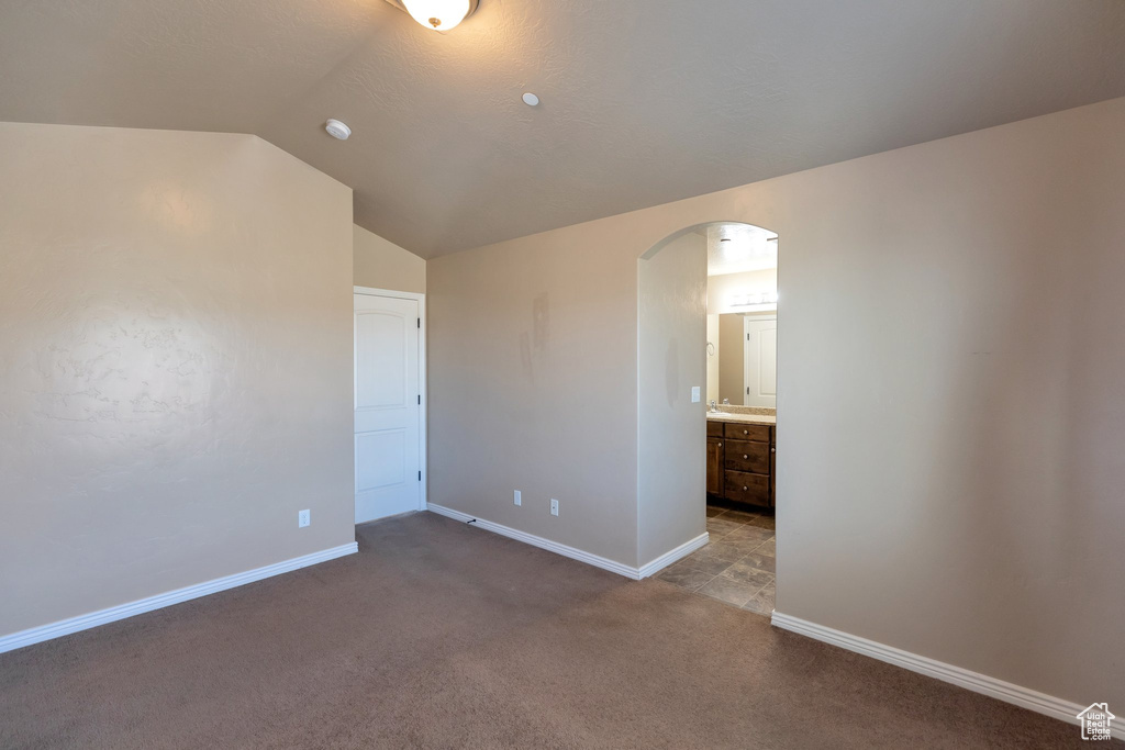 Unfurnished bedroom featuring dark carpet, ensuite bath, and vaulted ceiling