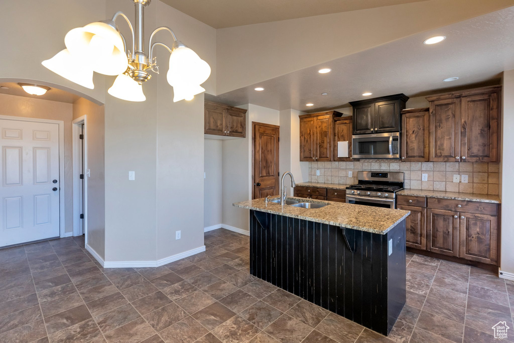 Kitchen featuring light stone countertops, stainless steel appliances, a kitchen island with sink, sink, and decorative light fixtures