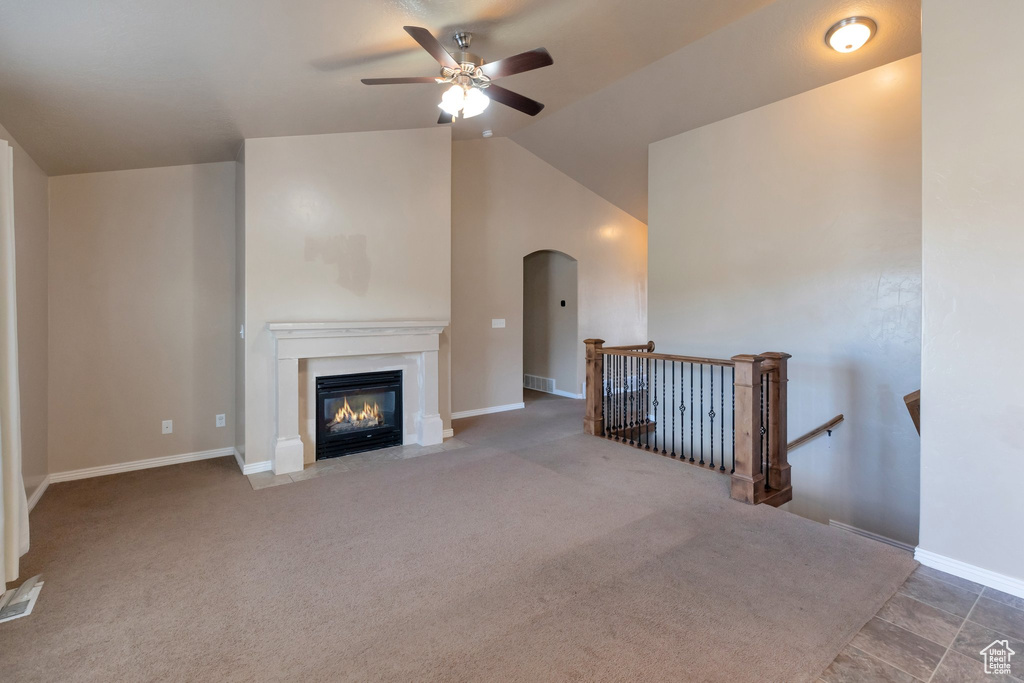 Unfurnished living room featuring dark colored carpet, ceiling fan, and vaulted ceiling
