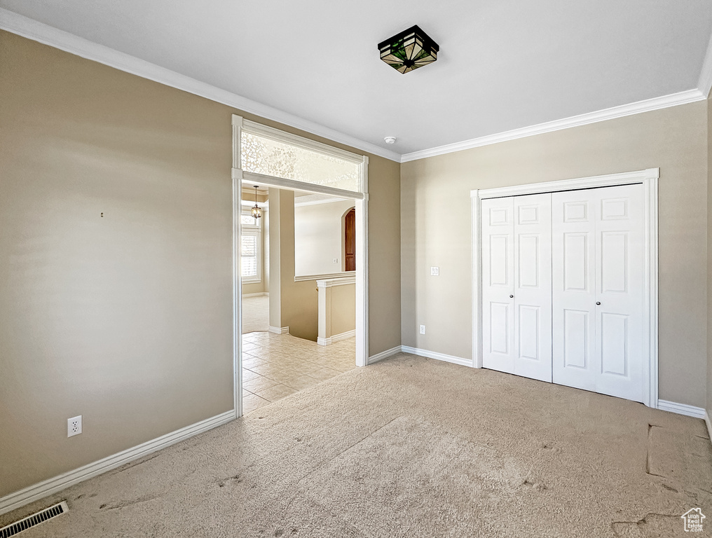 Unfurnished bedroom with ornamental molding, light colored carpet, and a closet