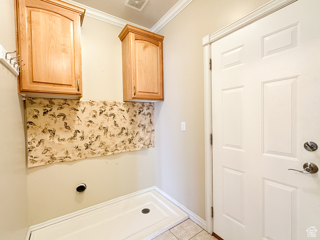 Clothes washing area with cabinets, ornamental molding, and light tile floors