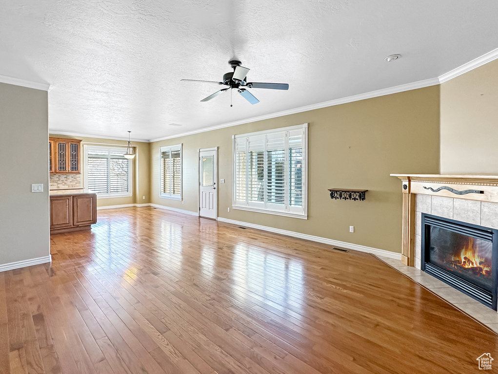 Unfurnished living room with a fireplace, crown molding, ceiling fan, and light wood-type flooring
