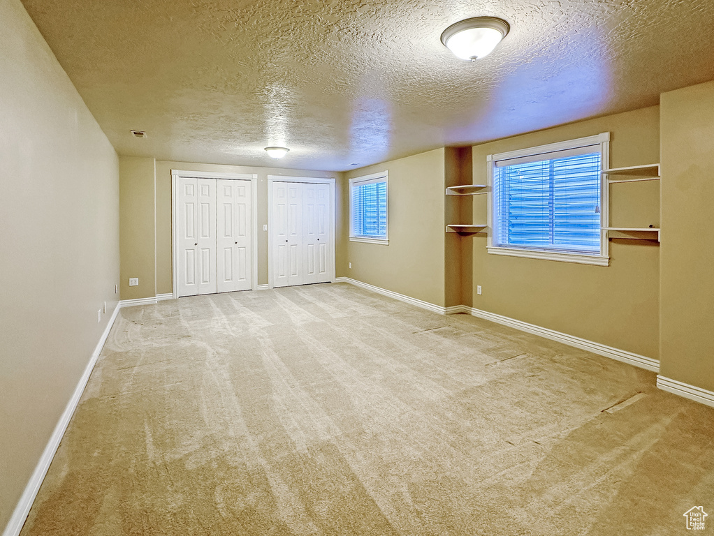 Unfurnished bedroom with light colored carpet, a textured ceiling, and two closets