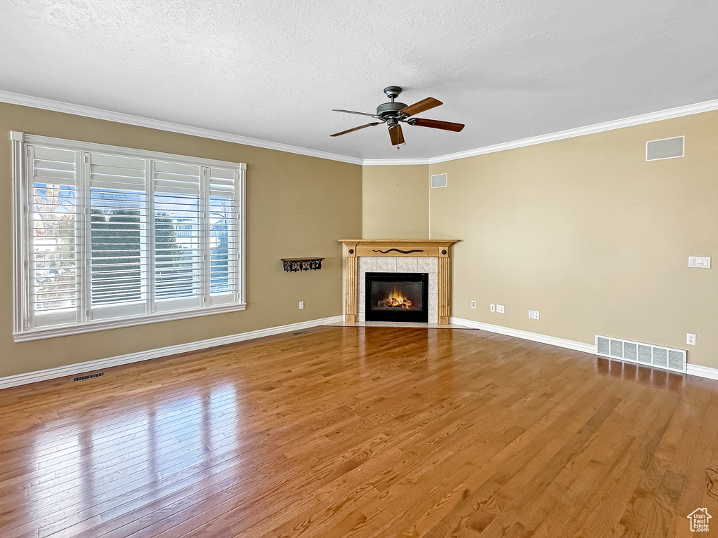 Unfurnished living room with a tiled fireplace, light hardwood / wood-style flooring, crown molding, and ceiling fan