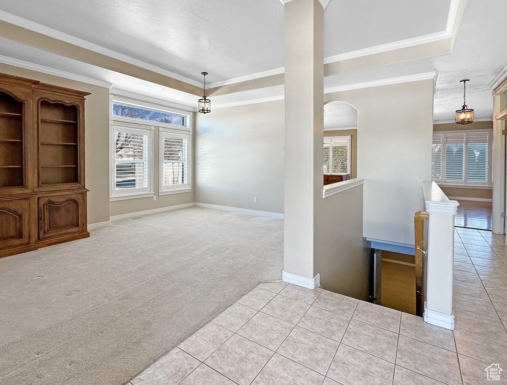 Empty room featuring a tray ceiling, light tile floors, and crown molding