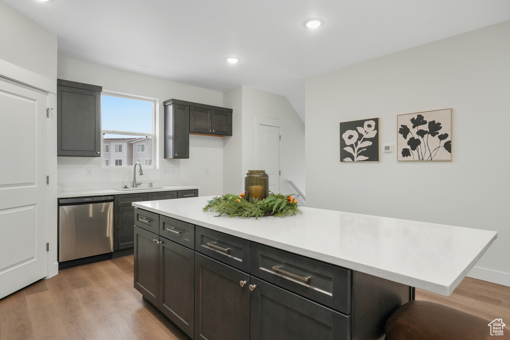 Kitchen featuring light hardwood / wood-style flooring, a kitchen island, a kitchen bar, sink, and stainless steel dishwasher