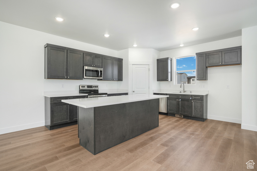 Kitchen with sink, a kitchen island, stainless steel appliances, and light wood-type flooring