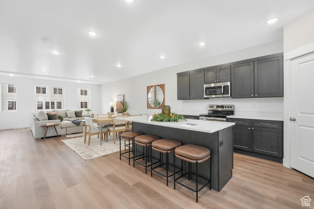 Kitchen with a kitchen island, appliances with stainless steel finishes, light hardwood / wood-style floors, and a kitchen breakfast bar
