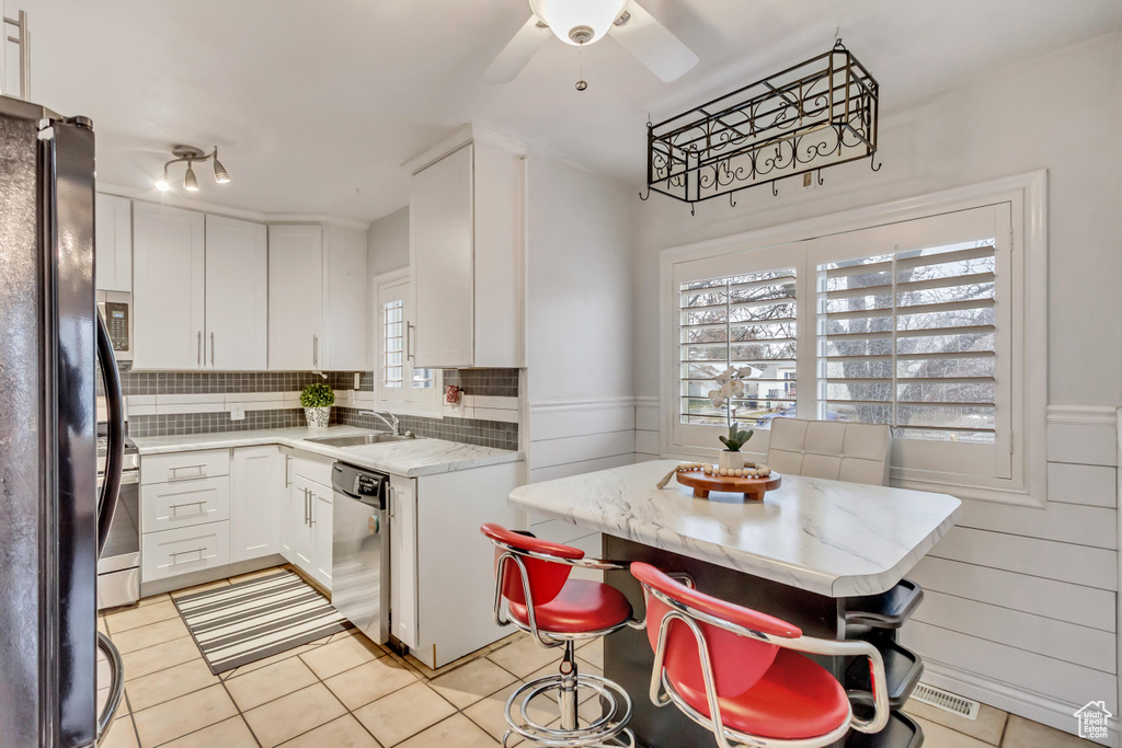 Kitchen with tasteful backsplash, white cabinetry, a breakfast bar, and light tile floors