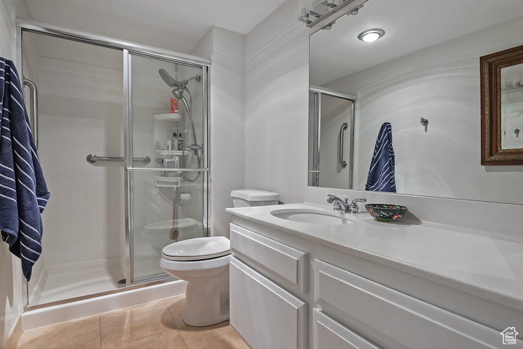 Bathroom with tile floors, toilet, a shower with shower door, and vanity with extensive cabinet space