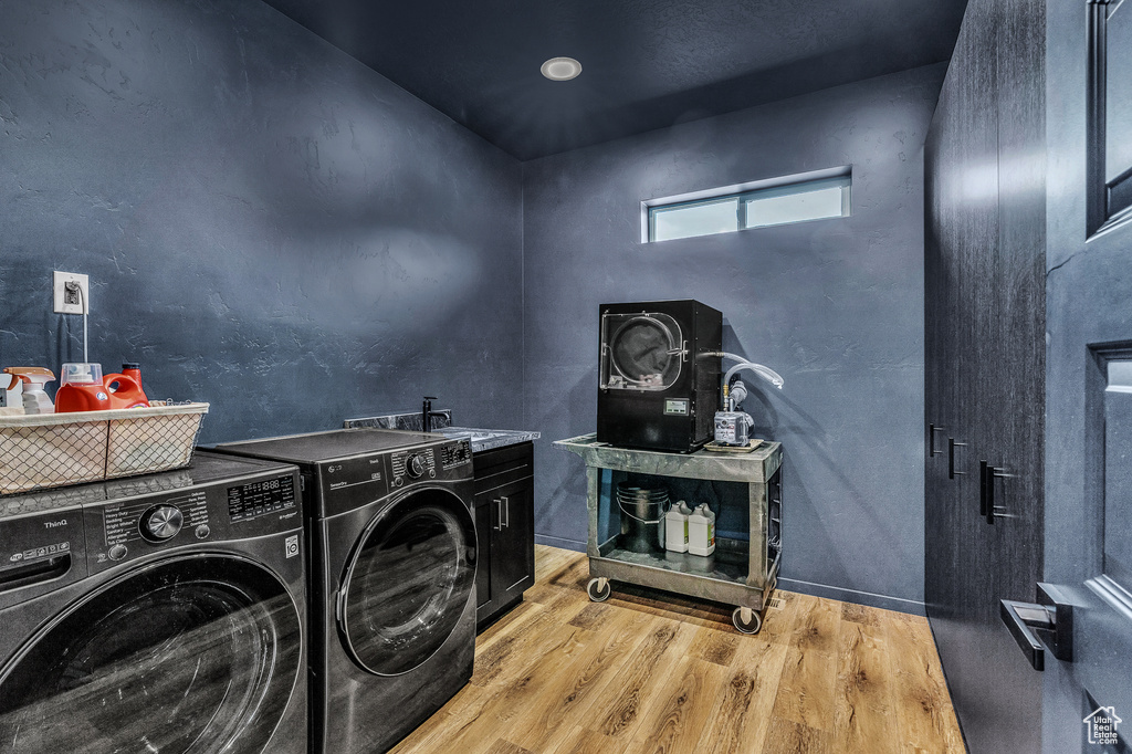 Washroom with cabinets, light hardwood / wood-style flooring, sink, and washing machine and clothes dryer