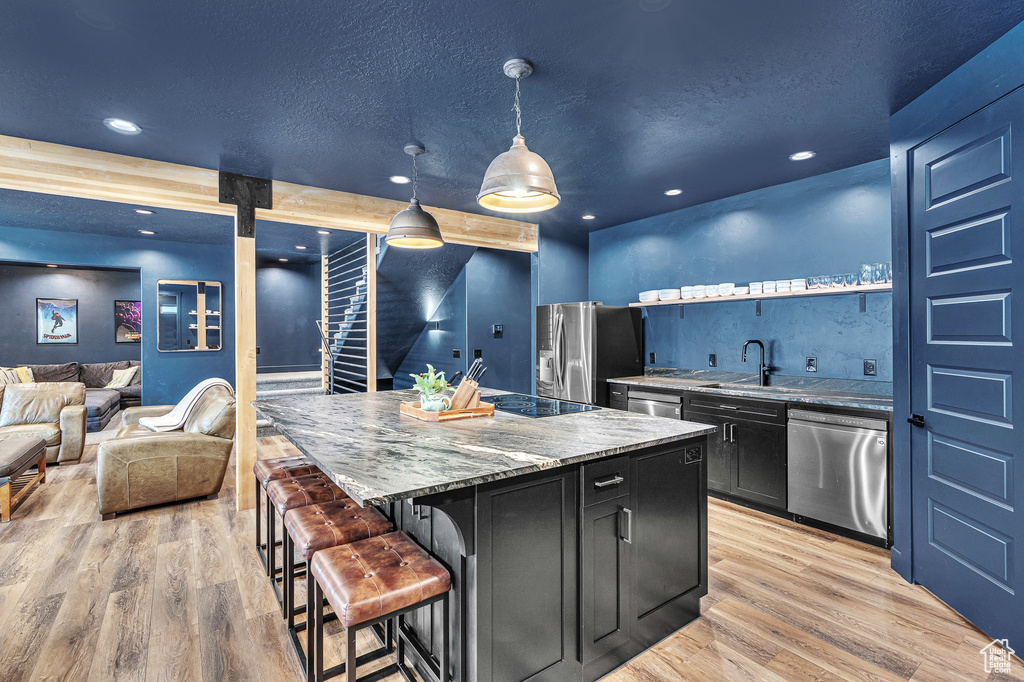 Kitchen with a kitchen island, appliances with stainless steel finishes, light hardwood / wood-style floors, a kitchen breakfast bar, and decorative light fixtures