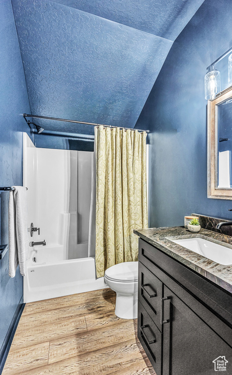 Full bathroom featuring shower / tub combo, vanity, vaulted ceiling, hardwood / wood-style flooring, and toilet