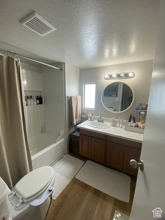 Full bathroom with toilet, hardwood / wood-style floors, a textured ceiling, shower / bathtub combination with curtain, and large vanity