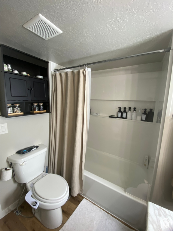 Bathroom featuring toilet, shower / bath combo, a textured ceiling, and wood-type flooring
