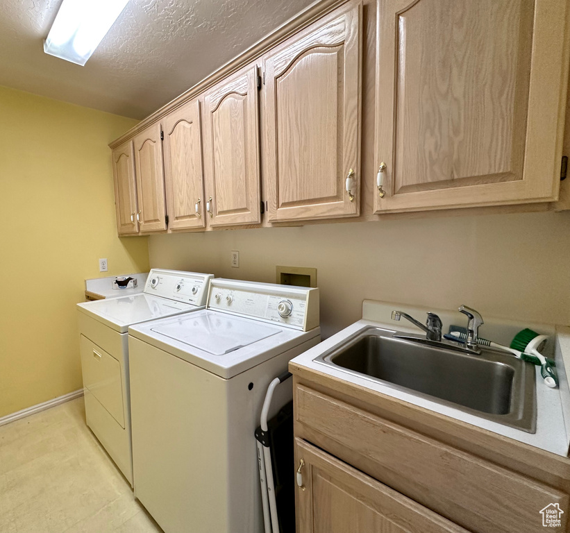 Laundry room featuring sink, washer and dryer, a textured ceiling, and cabinets