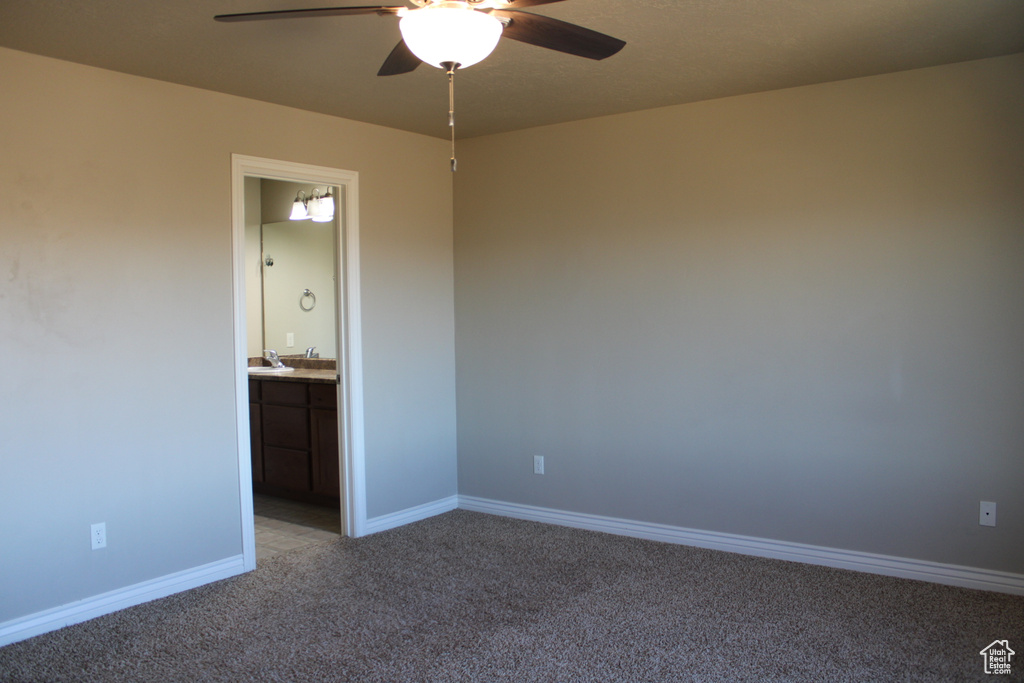 Unfurnished bedroom featuring dark carpet, ensuite bathroom, and ceiling fan