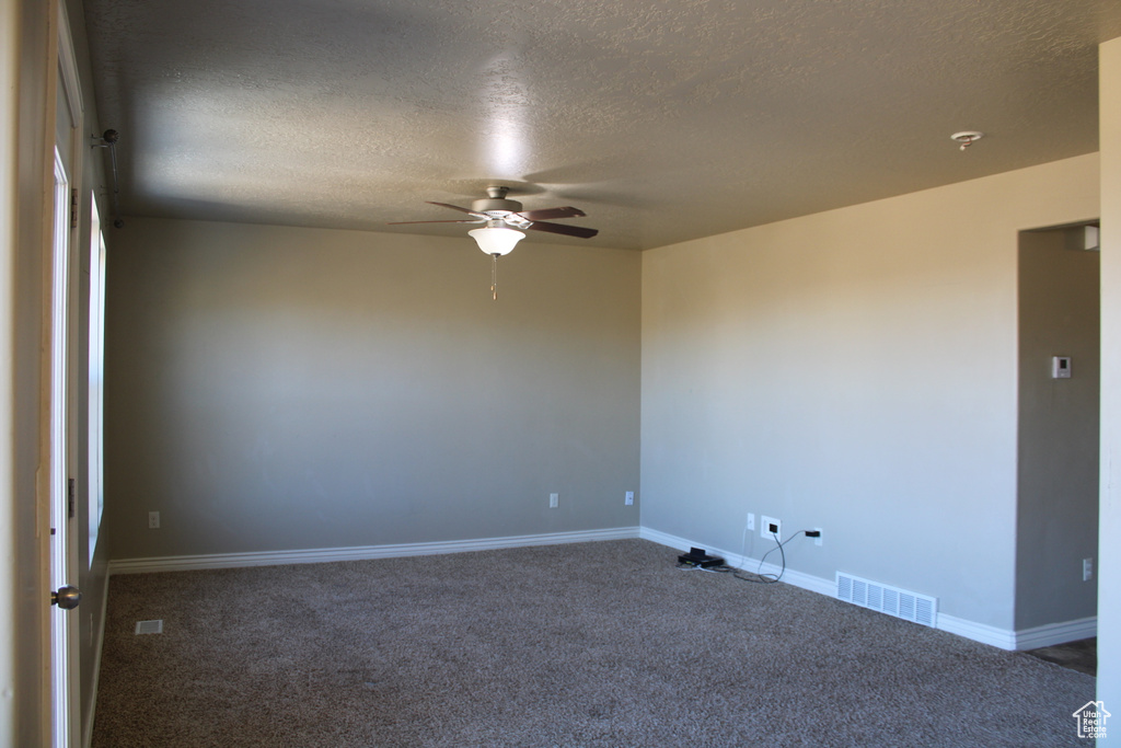 Empty room featuring dark colored carpet, ceiling fan, and a textured ceiling