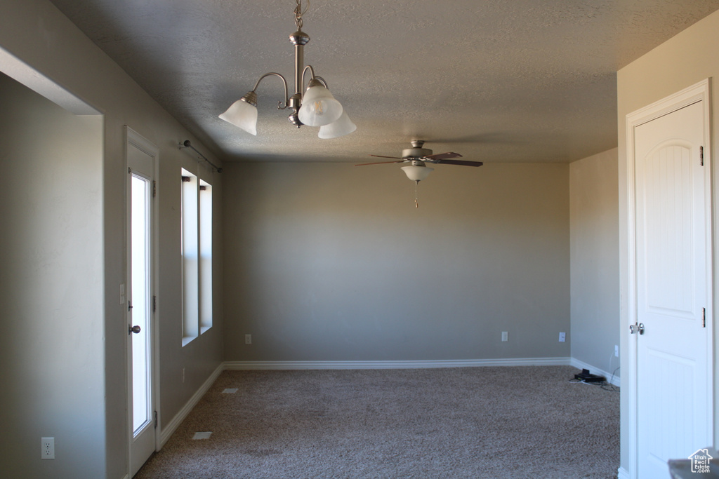 Spare room with dark colored carpet, ceiling fan with notable chandelier, and a textured ceiling
