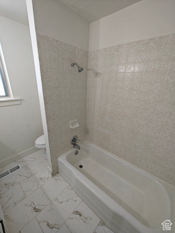 Bathroom with tiled shower / bath combo, tile flooring, a textured ceiling, and toilet