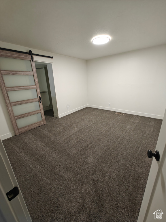 Empty room featuring a barn door and dark carpet