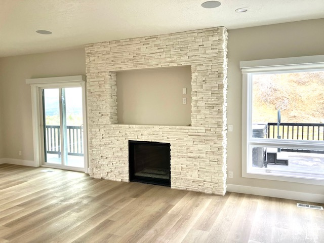 Unfurnished living room with light hardwood / wood-style floors and a stone fireplace