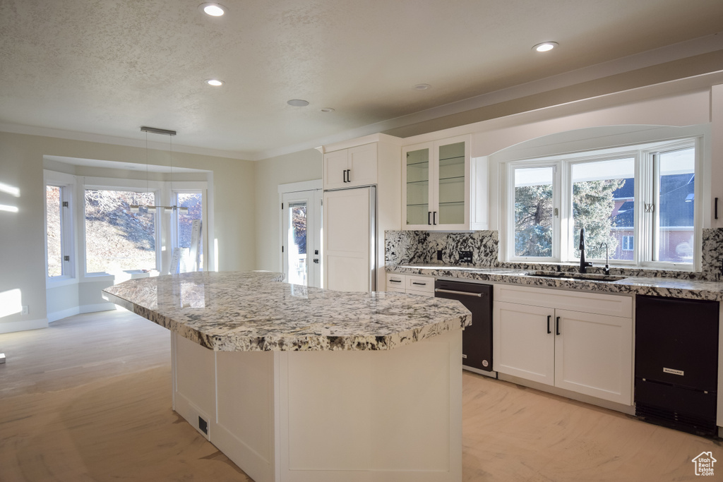 Kitchen with a kitchen island, dishwasher, backsplash, and white cabinets