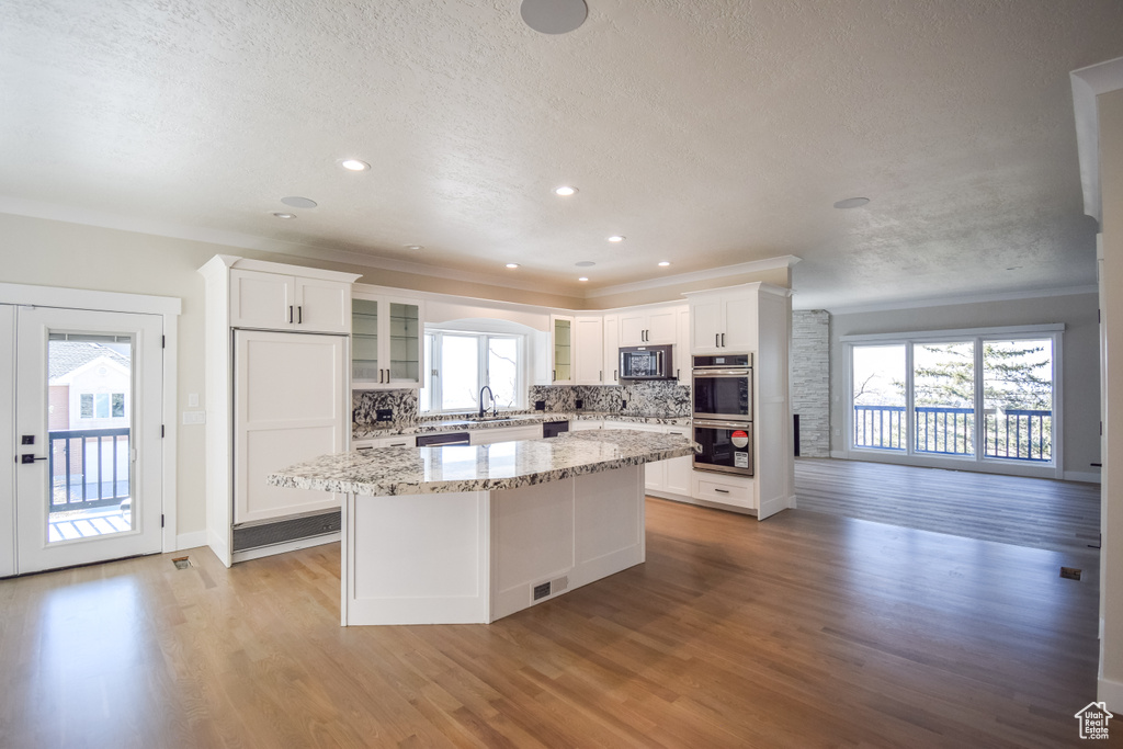 Kitchen featuring light hardwood / wood-style floors, a healthy amount of sunlight, backsplash, and white cabinets